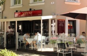 Außenansicht eines Cafés namens Va Bene mit Schanigarten und Gästen an Tischen.