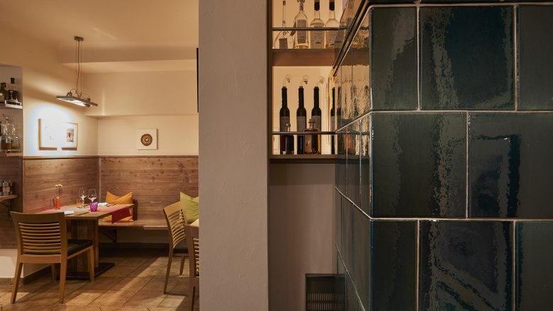 Gemütliche Stube mit Holzmöbeln, Kachelofen und Flaschenregal.