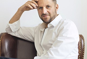Mann mit weißem Hemd in Denkerpose auf Stuhl.