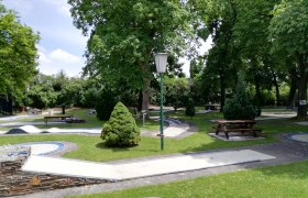 Minigolfplatz mit Bäumen und Bänken in einem Park.