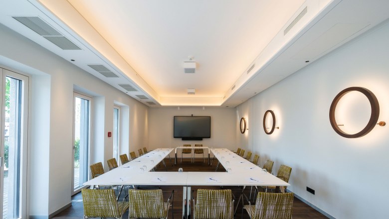 Modern seminar room with U-shaped table arrangement, chairs, a large screen and decorative wall lamps.