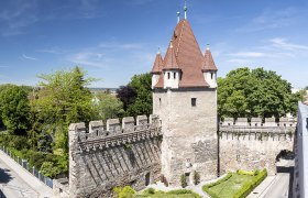 Reckturm mit rotem Dach und Steinmauer, umgeben von B&auml;umen und Stra&szlig;en.