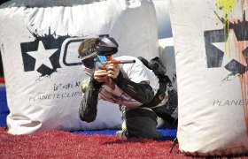 Ein Paintball-Spieler in Schutzkleidung zielt mit einer Paintball-Waffe hinter einer aufblasbaren Deckung.
