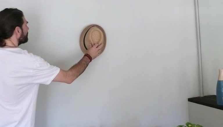 Person hangs straw hat on a wall with several hats.