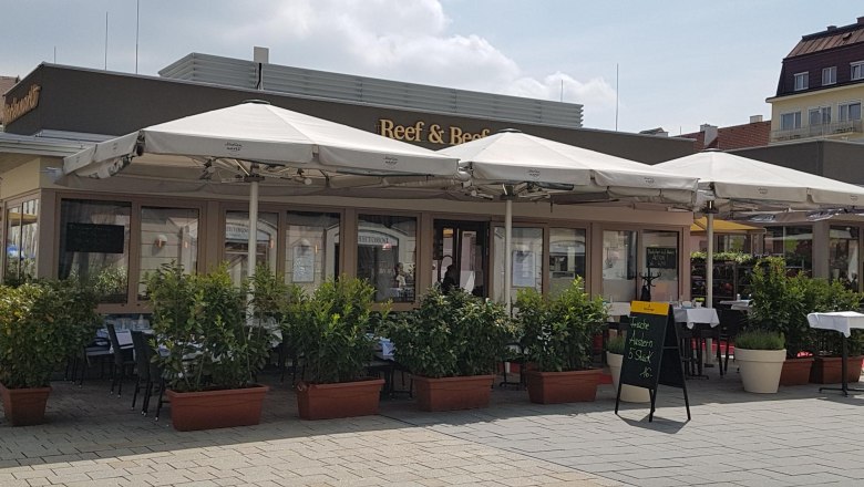 Exterior view of a restaurant with sidewalk seating and umbrellas.