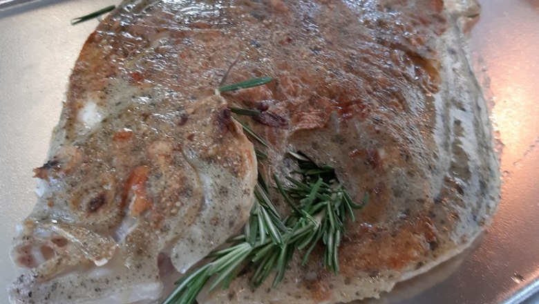 Baked fish with rosemary on a baking tray.