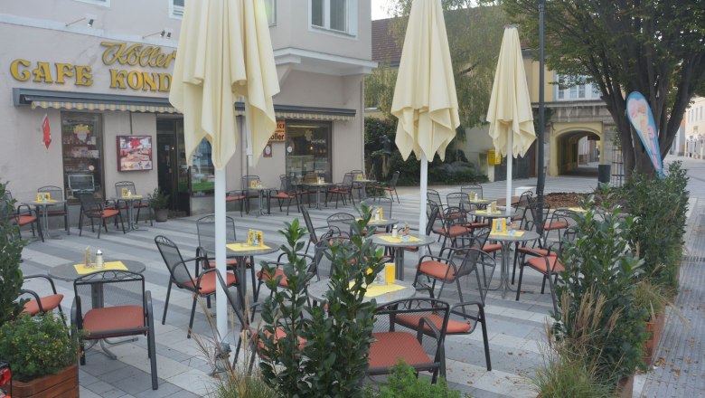 An empty pavement garden with tables and chairs in front of a café with yellow parasols.