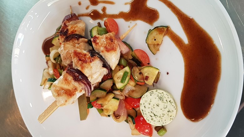 Grilled meat skewers with vegetables and herb butter on a white plate.