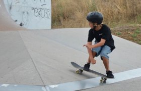 Ein Kind mit Helm fährt auf einem Skateboard in einem Skatepark.