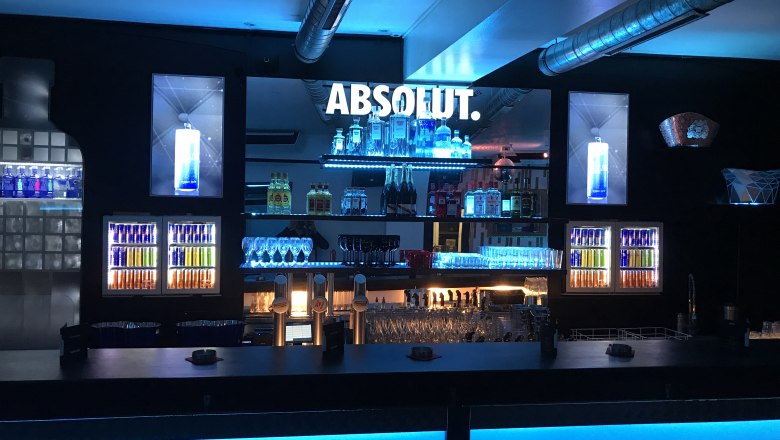 A stylish bar with blue lighting and various bottles and glasses on shelves.