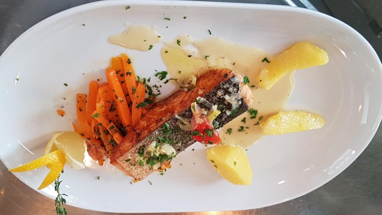 A plate with fish fillet, carrots, potatoes and a slice of lemon, garnished with herbs and sauce.