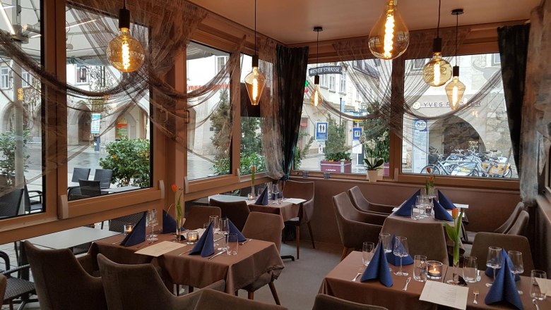 Interior view of a stylishly furnished restaurant with set tables and large windows.