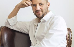 Mann mit weißem Hemd in Denkerpose auf Stuhl.