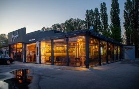 Außenansicht eines modernen Restaurants bei Dämmerung mit großen Glasfenstern und warmem Licht.