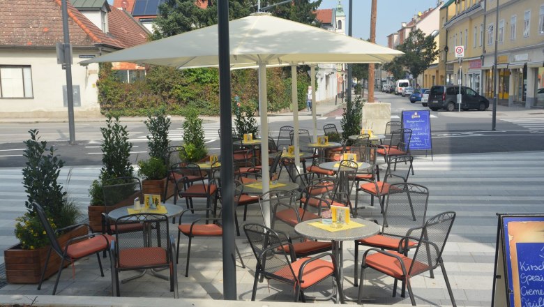 An empty pavement garden with tables, chairs and parasols on a paved area in an urban environment.