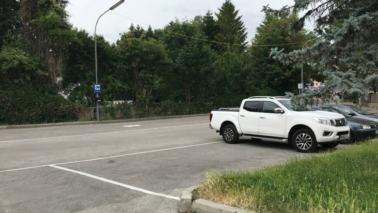 An empty parking lot with a white pickup truck and a car, surrounded by trees.