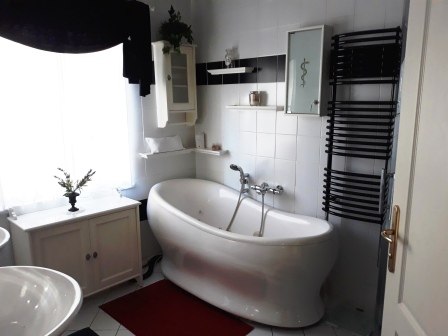 Modernes Badezimmer mit freistehender Badewanne, weiß gefliest, schwarzer Handtuchhalter und roter Teppich.