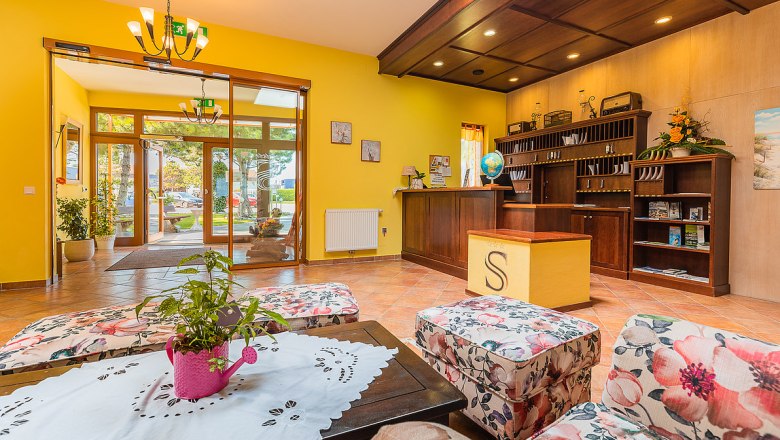 Hotelrezeption mit gelben Wänden, Holzmöbeln und Blumenmuster-Sesseln.