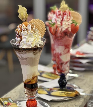 Two decorative ice cream sundaes with whipped cream, waffles and fruit on a table.