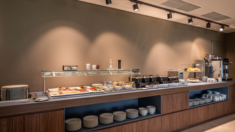 Ein Frühstücksbuffet mit verschiedenen Speisen und Geschirr in einem modernen Raum.