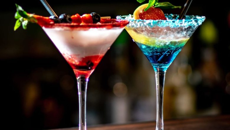 Zwei bunte Cocktails in Martini-Gläsern mit Beeren und Minze dekoriert.