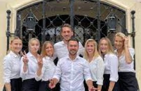 Gruppe von acht Personen in weißer Kleidung vor einem Restaurant namens Novecento.