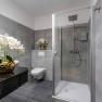 Modernes Badezimmer mit grauen Fliesen, Dusche, Toilette und Orchideen in goldenen Vasen.