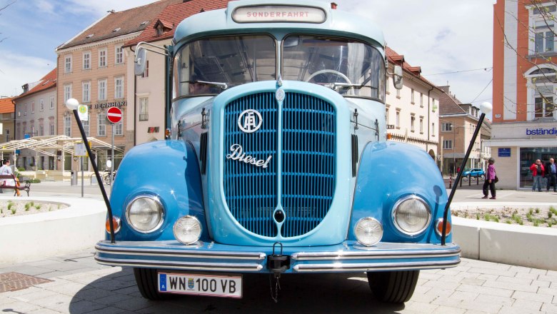 Ein blauer Oldtimer-Bus aus dem Jahr 1961 steht auf einem Platz vor Gebäuden.
