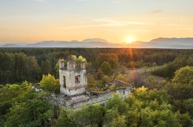 Verfallenes Gebäude im Grünen, im Hintergrund Sonnenuntergang über Bergen.