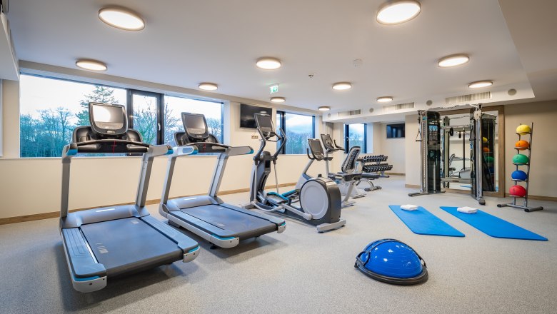 Fitnessraum mit Laufbändern, Crosstrainer, Hanteln und Gymnastikmatten.