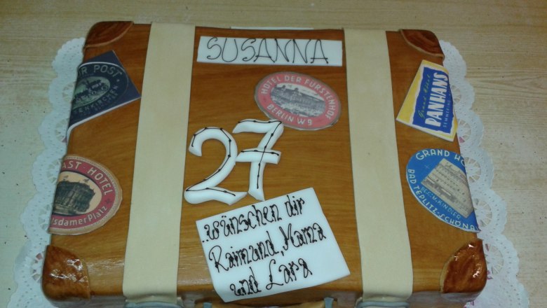 Eine Torte in Form eines Koffers mit Aufklebern und der Zahl 27.