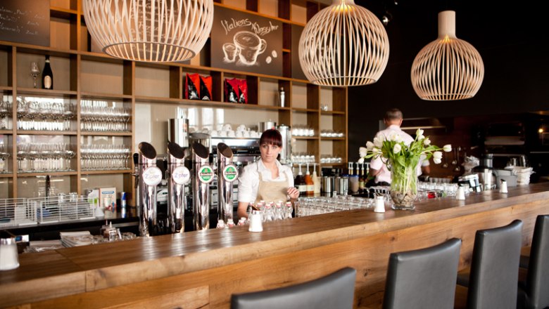 Moderne Bar mit Holztheke, Zapfhähnen und dekorativen Lampen.