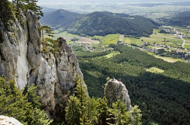 Person steht auf Felsnadel mit Panoramablick über Wienerwald und Felder.