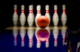 Eine Bowlingkugel rollt auf eine Gruppe von Kegeln zu.