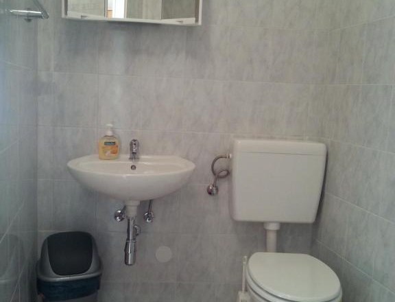 Kleines Badezimmer mit Waschbecken, Spiegel, Toilette und Mülleimer.