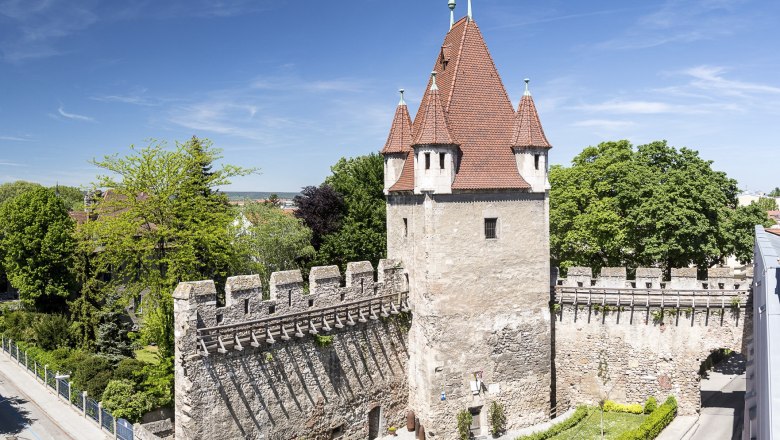 Reckturm mit rotem Dach und Steinmauer, umgeben von Bäumen und Straßen.