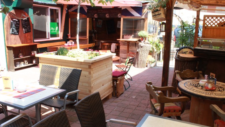 A cozy pub garden with tables, chairs and plants under a sun canopy.