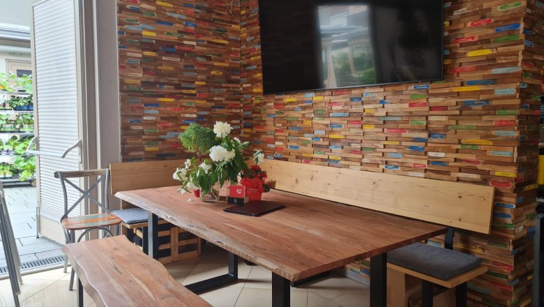 Innenansicht eines Pubs mit Holztisch, Bank und bunter Holzverkleidung an der Wand.