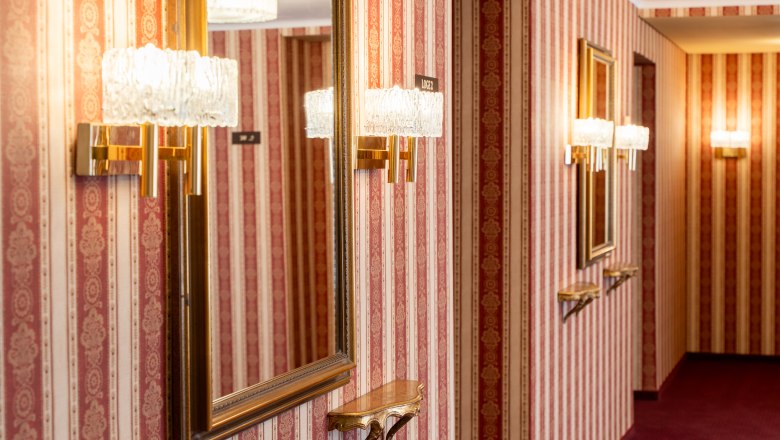 Nostalgischer Gang im Stadttheater Wiener Neustadt mit rot-goldener Tapete, Spiegeln und Kristallwandleuchten
